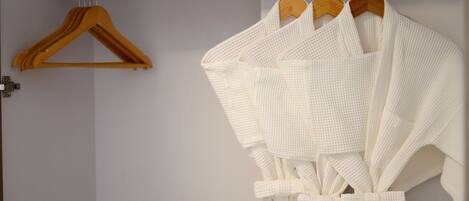 A bathroom with a white towel rack holding three white towels and a wooden hanger.