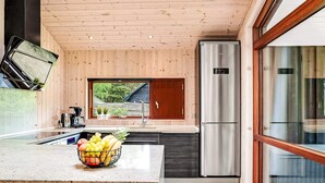 A modern kitchen with a wooden ceiling, a stainless steel refrigerator, and a large window overlooking a garden. - 5 Star Holiday Home in Vaeggerlose (Vaeggerlose)