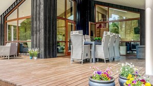 A modern outdoor deck with a wooden floor, wicker furniture, and potted plants. - 5 Star Holiday Home in Vaeggerlose (Vaeggerlose)