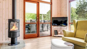 A cozy living room with a wood-burning stove, a comfortable armchair, and a television. - 5 Star Holiday Home in Vaeggerlose (Vaeggerlose)