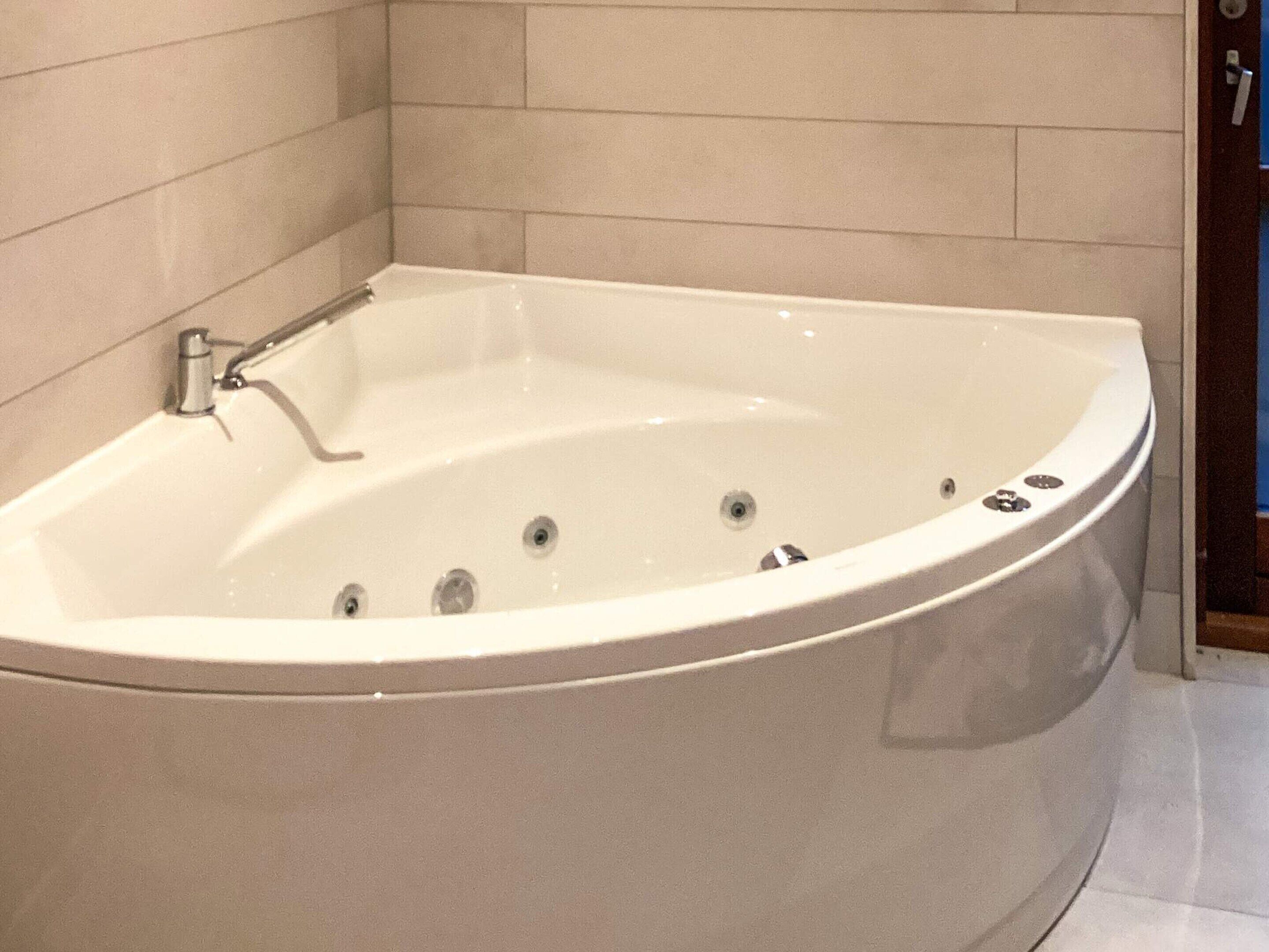 A large, freestanding bathtub in a bathroom with tiled walls and a wooden floor.