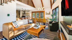 A spacious living area with a high ceiling, wooden beams, a modern fireplace, and a dining area with yellow chairs. - Slope View Chalet Hot Tub, Firepit, Family Fun (McGaheysville)