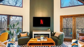 A living room with a fireplace, a television mounted above it, and a large window. - Slope View Chalet Hot Tub, Firepit, Family Fun (McGaheysville)