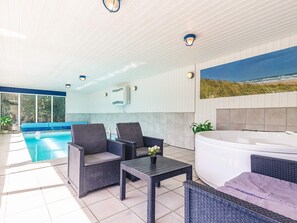 A modern indoor pool area with a hot tub, wicker furniture, and a large window overlooking the ocean. - 4 Star Holiday Home in Vaeggerlose (Vaeggerlose)
