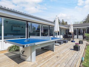 A pool table in an outdoor patio area with a wooden deck, outdoor furniture, and a building with large windows and doors. - 4 Star Holiday Home in Vaeggerlose (Vaeggerlose)