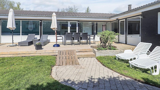 Een modern huis met een patio, buitenmeubilair, een houten terras en een tuin.
