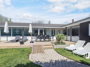 A modern house with a patio area featuring outdoor furniture, a wooden deck, and a garden. - 4 Star Holiday Home in Vaeggerlose (Vaeggerlose)