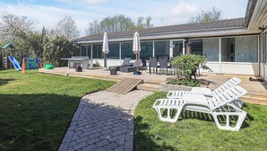 Een modern huis met een patio met buitenmeubilair, een kinderspeelplaats en een verzorgd gazon.