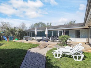 A modern house with a patio area featuring outdoor furniture, a children's playset, and a well-maintained lawn. - 4 Star Holiday Home in Vaeggerlose (Vaeggerlose)