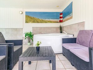 A sunlit outdoor seating area with wicker furniture, a hot tub, and a beach mural on the wall. - 4 Star Holiday Home in Vaeggerlose (Vaeggerlose)
