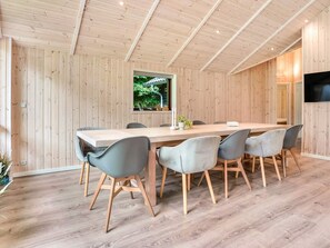 Un espace repas moderne avec une table et des chaises en bois, une fenêtre donnant sur un paysage verdoyant et un téléviseur à écran plat fixé au mur.