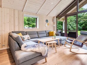 A modern living room with a sectional sofa, a small table, and a rocking chair. - 5 Star Holiday Home in Vaeggerlose (Vaeggerlose)