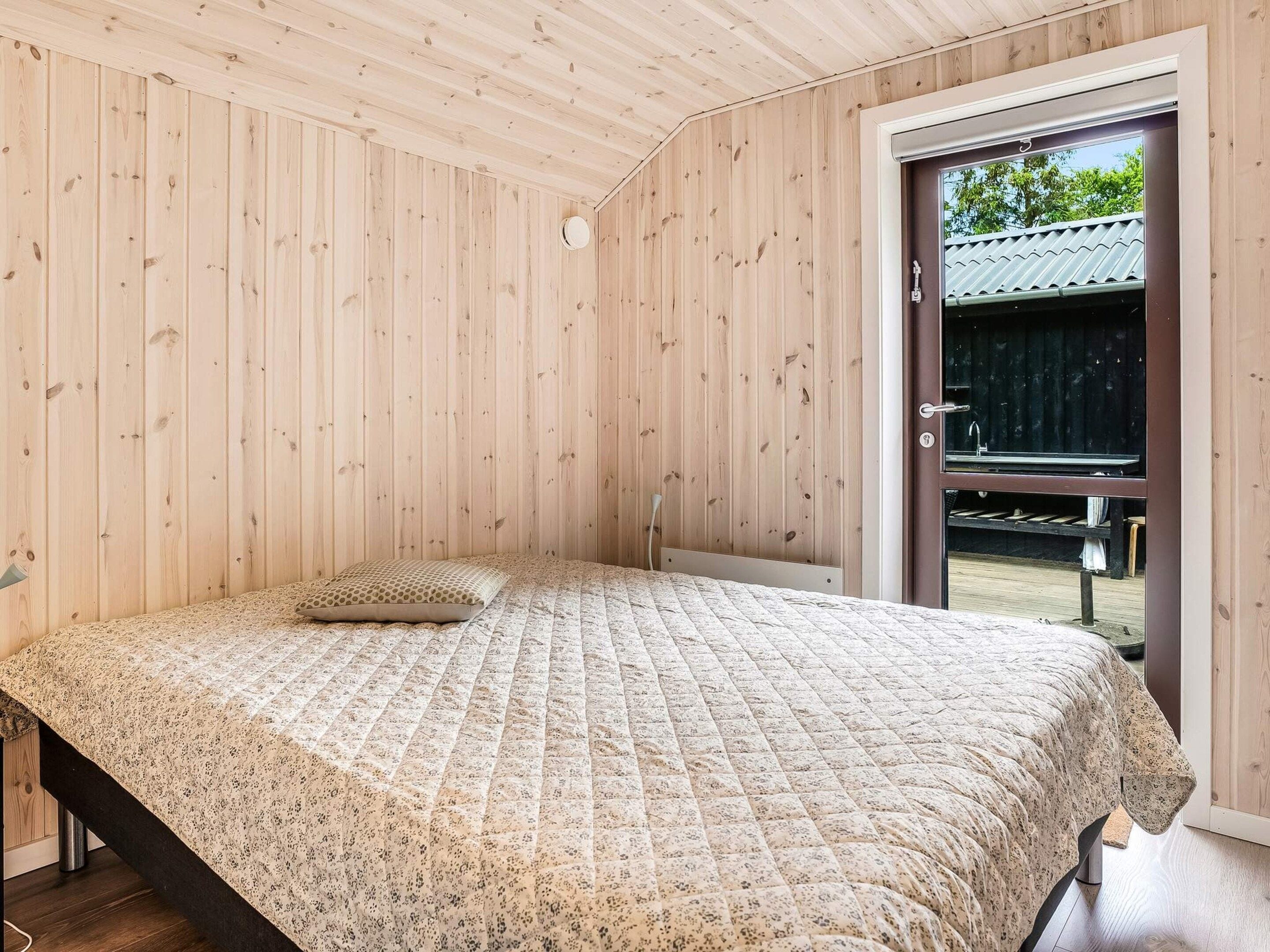 A bedroom with a bed, a wooden ceiling, and a door leading outside.