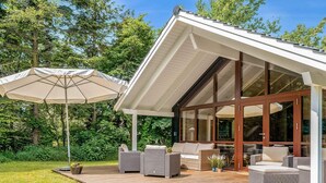 A modern house with a wooden deck, outdoor furniture, and large windows. - 5 Star Holiday Home in Vaeggerlose (Vaeggerlose)