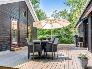 A wooden deck with a table and chairs, a large umbrella, and a potted plant. - 5 Star Holiday Home in Vaeggerlose (Vaeggerlose)