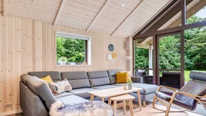 A modern living room with a grey sectional sofa, a small wooden table, a fluffy throw blanket, and a rocking chair. - 5 Star Holiday Home in Vaeggerlose (Vaeggerlose)
