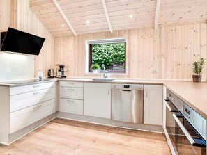 A modern kitchen with wooden panel walls, a stainless steel dishwasher, and a window with a view of greenery. - 5 Star Holiday Home in Vaeggerlose (Vaeggerlose)