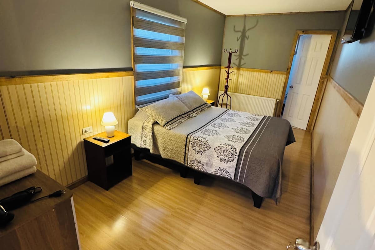A bedroom with a bed, bedside table, lamp, and a coat rack.