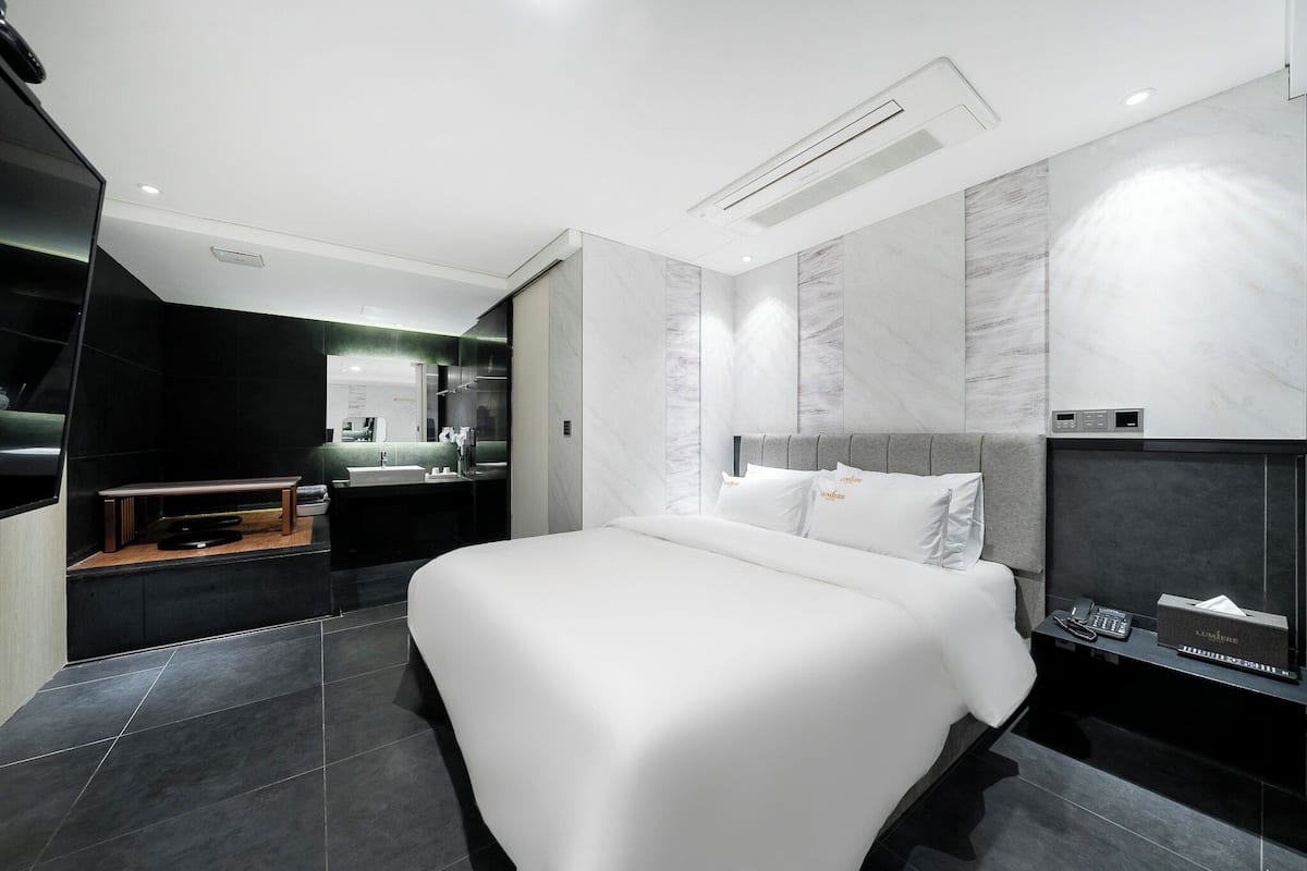 Quarto de hotel moderno com uma cama grande, uma toucador com espelho e uma televisão sobre um suporte de madeira.