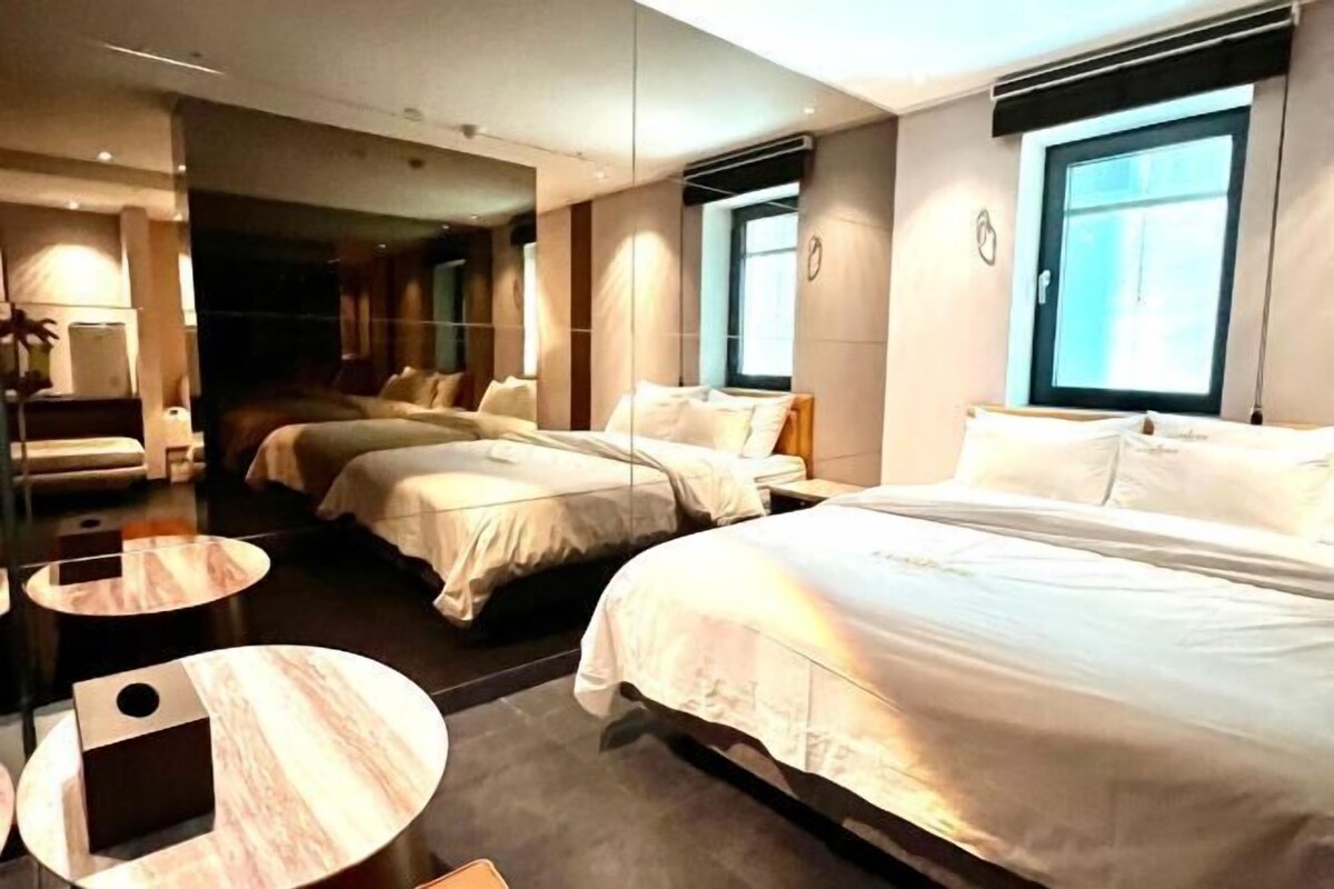A hotel room with two beds, a sitting area with a round table, and a large window providing natural light.