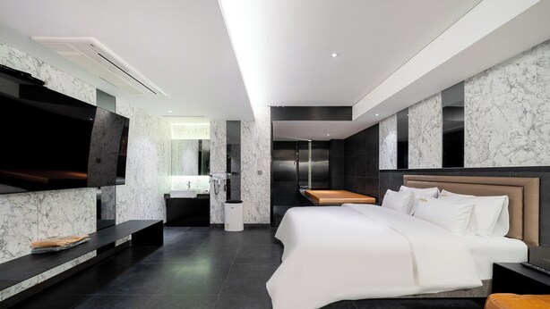 A modern hotel room with a large bed, a TV, a bathroom, and a marble wall. - Yeoksam Lumiere (Seoul)