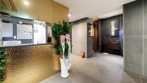 A reception area with a reception desk, a potted plant with a pink bow, a fire extinguisher, and a wall with a 'LUMIERE' sign. - Yeoksam Lumiere (Seoul)