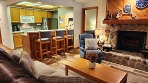 Ein gemütliches Wohnzimmer mit Kamin, eine Küchenzeile mit Holzschränken und ein Esstisch.