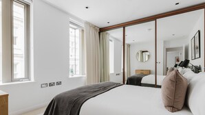 A modern hotel room with a large bed, a mirror, and a view of the city through the window.
