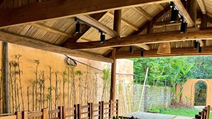 Un área de comedor al aire libre con madera, techos altos y plantas de bambú.