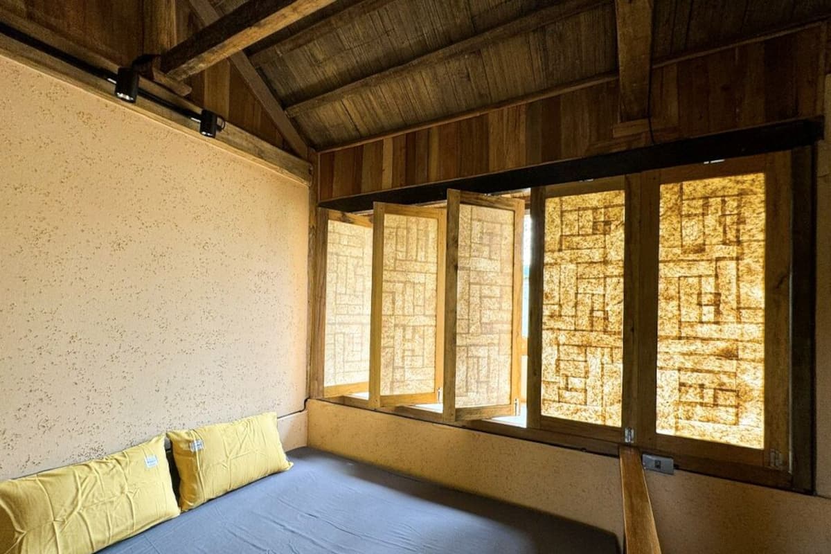 A room with a bed, wooden beams, and a window with a brick pattern.
