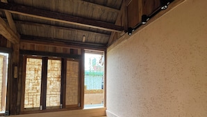 Una habitación con techo de madera, una cama con almohada amarilla, una ventana con vista a follaje, y una escalera que sube a un nivel superior.