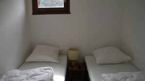 Una habitación de hotel pequeña y sencilla con dos camas, una mesita de noche con lámpara y una ventana con vistas a árboles.