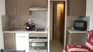Cocina compacta con lavavajillas, horno y microondas. Un televisor pequeño está sobre una encimera.