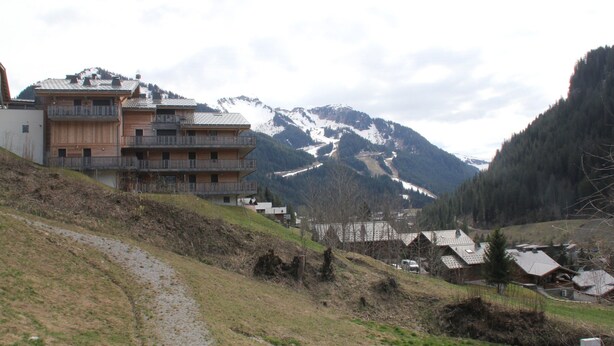 Un complejo turístico de montaña con edificios de madera, una pista de esquí y un sendero que sube.
