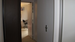 Un pasillo con una puerta cerrada, una silla y una pequeña mesa al fondo.