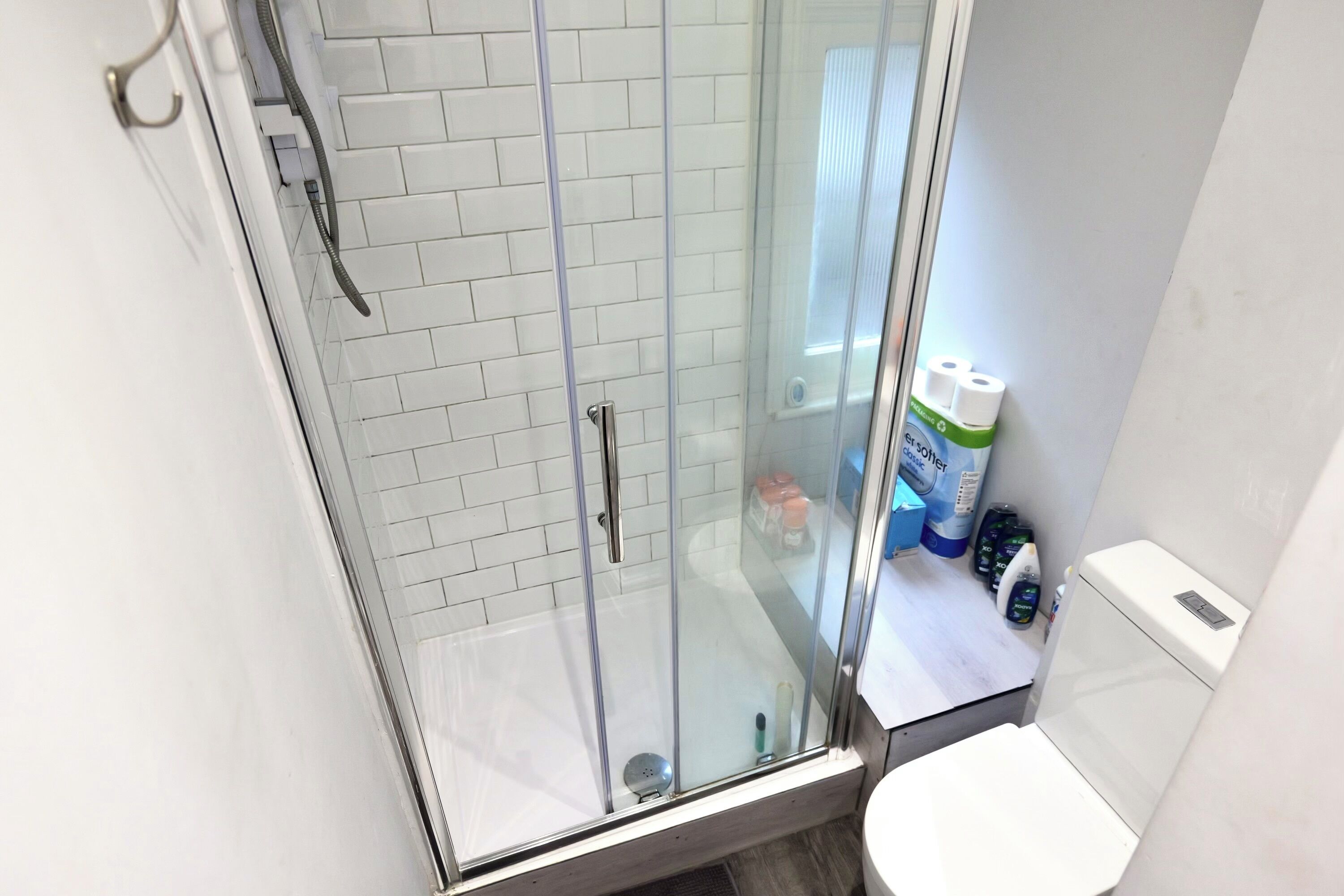A glass-enclosed shower with white tiled walls and a white toilet visible through the glass.