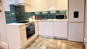 A modern kitchen with white cabinets, a stainless steel oven, a microwave, and a built-in dishwasher. - The Hampstead Hideaway (London)