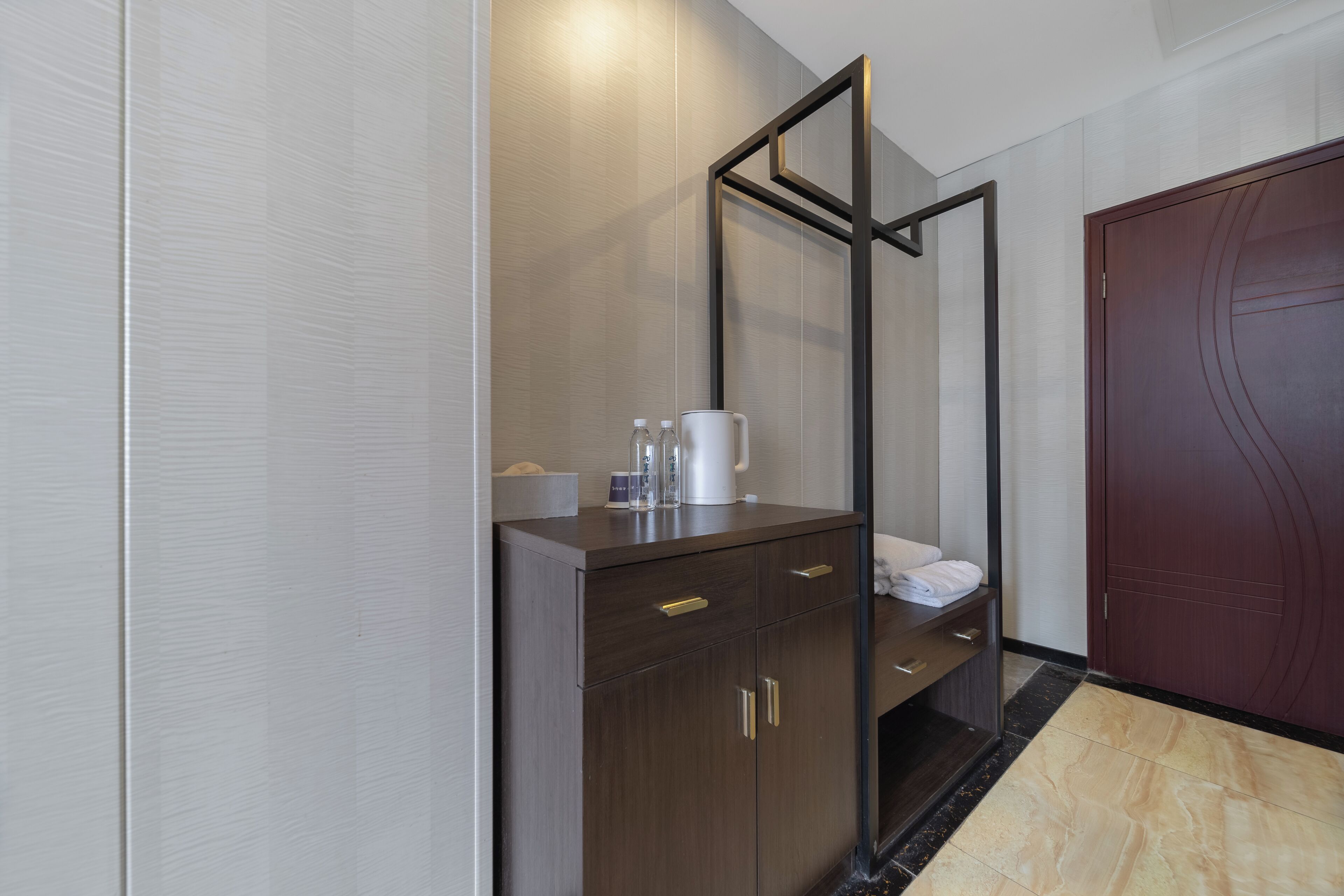 A modern hotel room with a wooden cabinet, a mirror, and a dark wooden door.