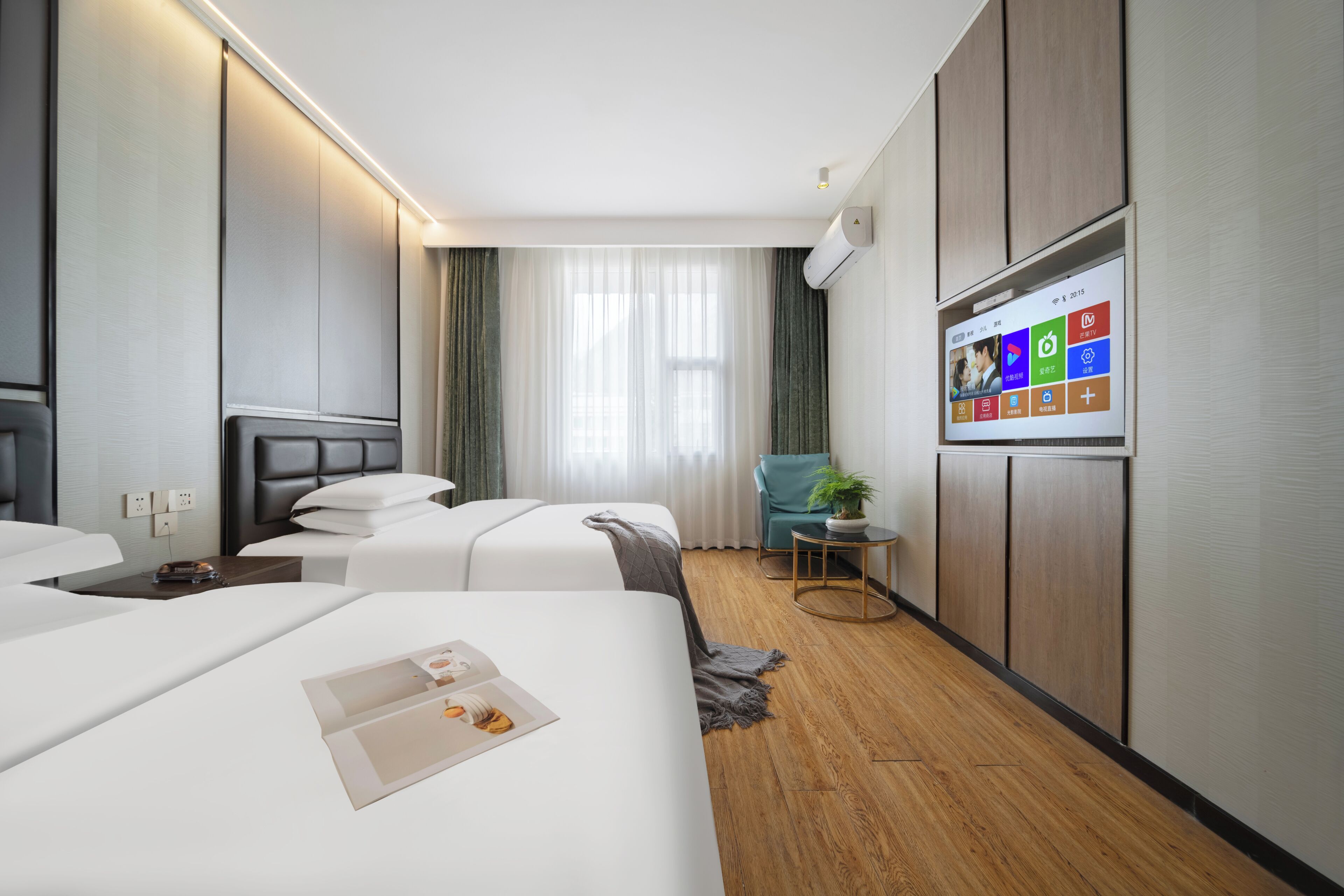 Habitación de hotel con dos camas, un televisor montado en la pared, una mesita con una planta y una ventana con cortinas.