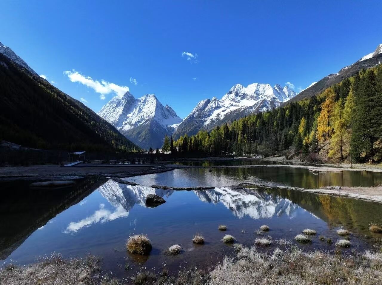 Un lago de montaña con reflejos, rodeado de montañas boscosas y cielos despejados.