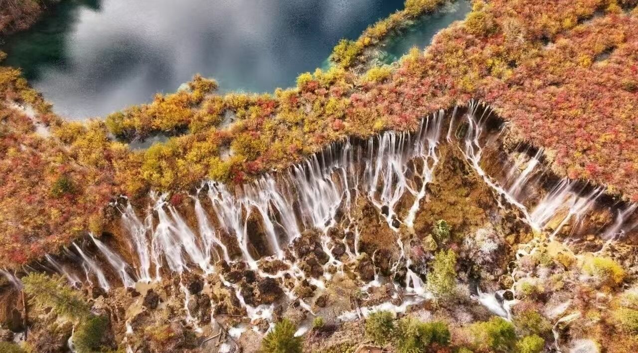 Uma cascata despencando sobre um penhasco rochoso, cercada por folhagem outonal.