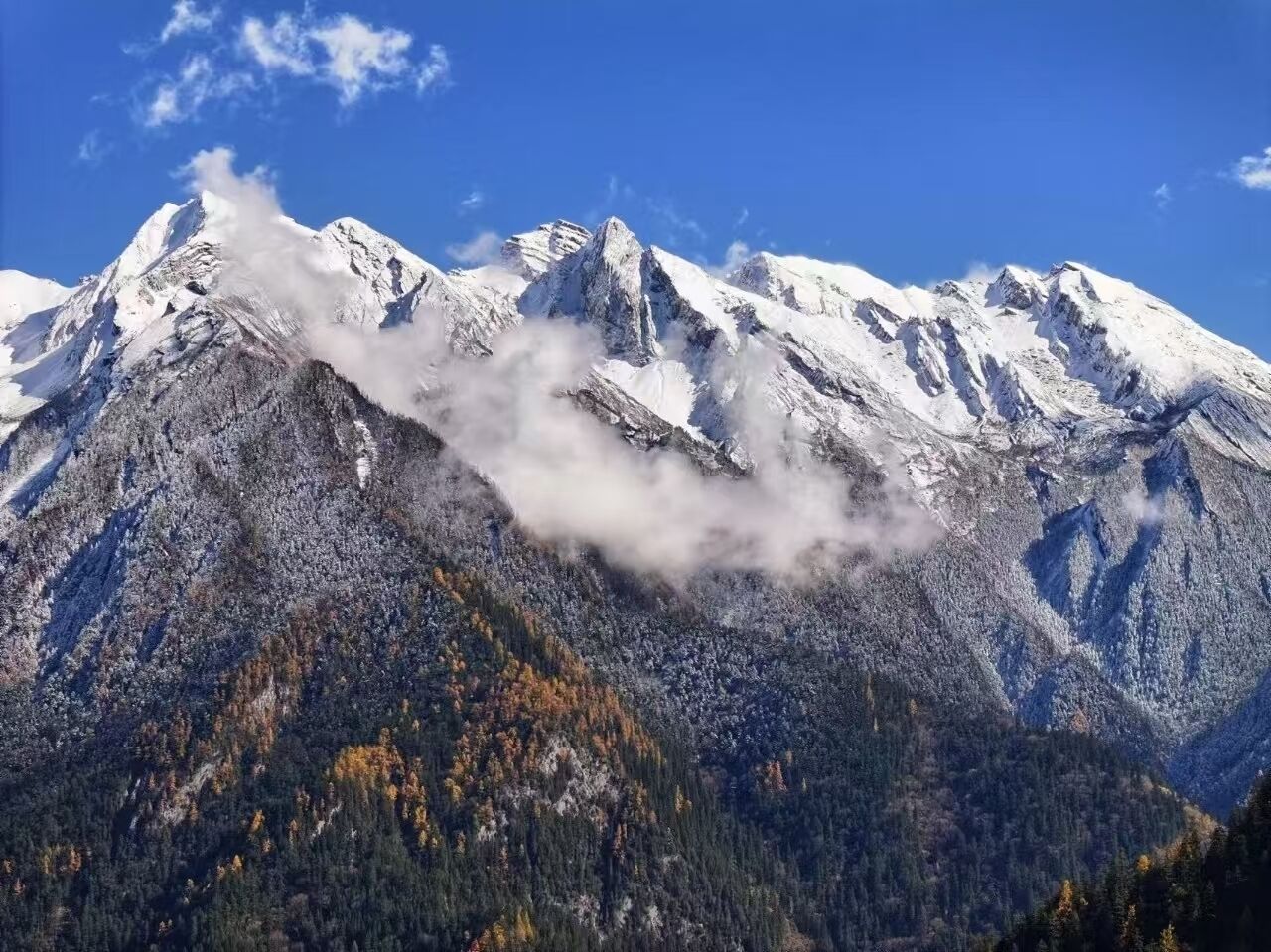 A mountain landscape with snow-covered peaks and a forested valley.