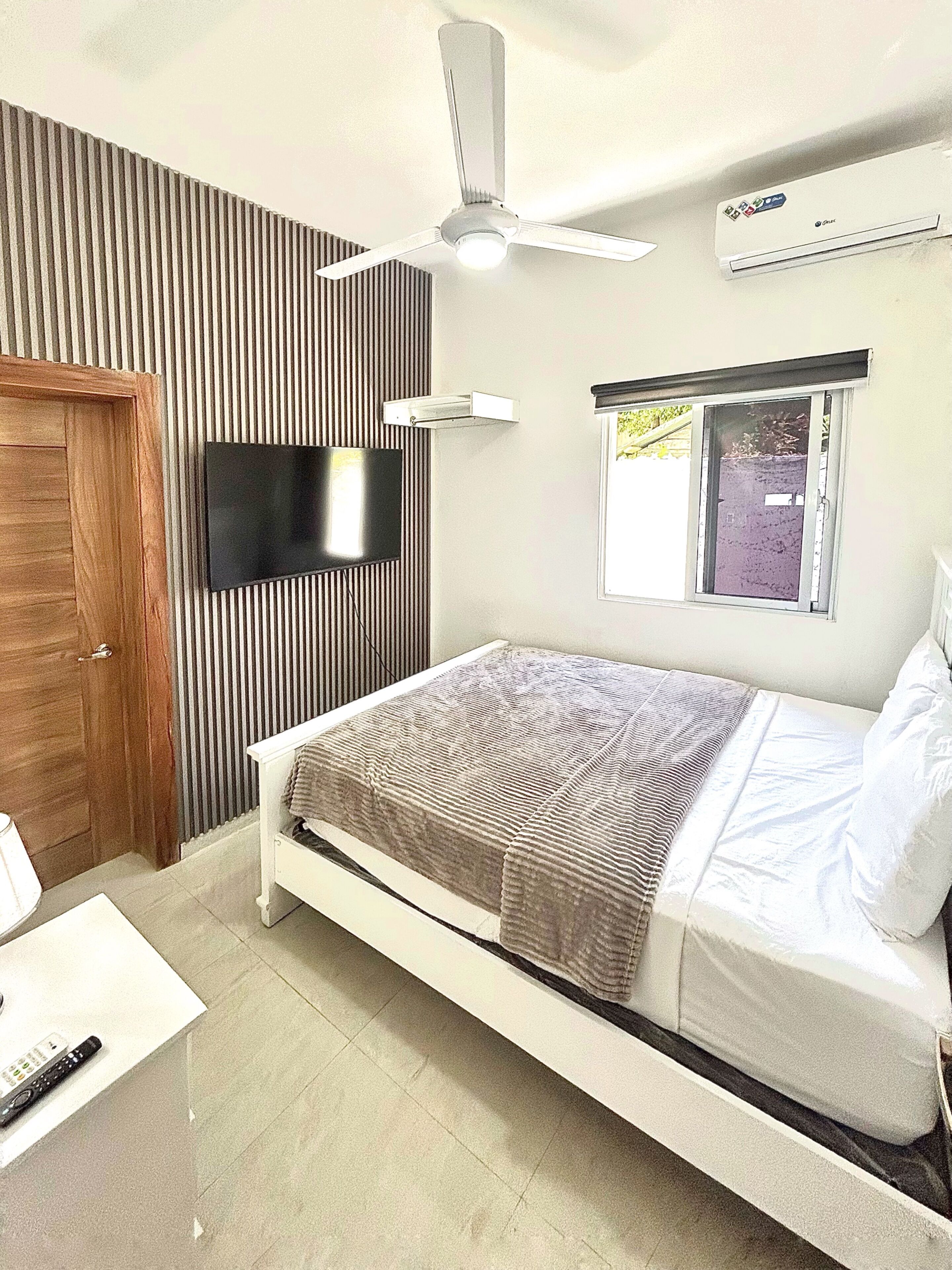 Une chambre à coucher comprenant un lit, un téléviseur, un ventilateur de plafond et un appareil de climatisation.