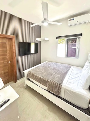 Quarto com cama, televisão, ventoinha no teto e ar condicionado.