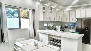 Ett modernt kök med vita skåp, en köksö med en diskho och hängande lampor.