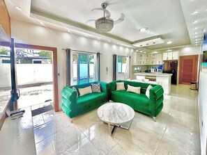 Uma sala de estar moderna com um sofá verde, uma mesa de centro redonda e uma cozinha ao fundo.