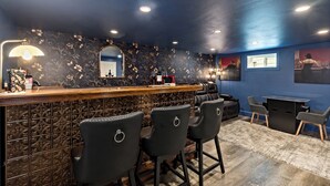 A bar area with a counter, three bar stools, a mirror, and a patterned wall.
