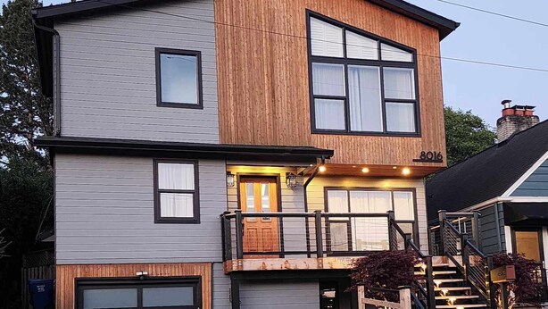 A two-story house with a garage, a wooden facade, and a balcony.