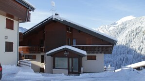 Eine Holzhütte mit geneigtem Dach und einem Balkon, umgeben von schneebedeckten Bergen.