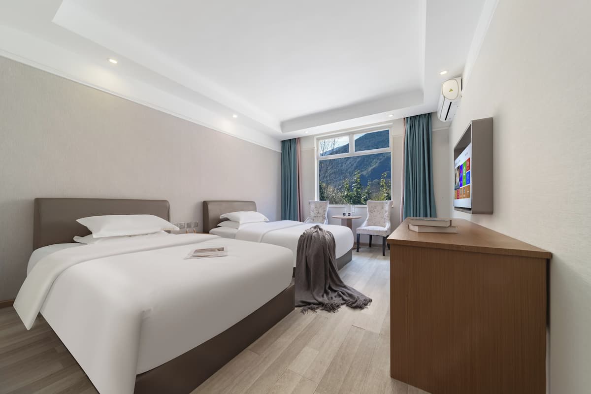 Ein Hotelzimmer mit zwei Betten, einem Schreibtisch, einem Stuhl und Bergblick.